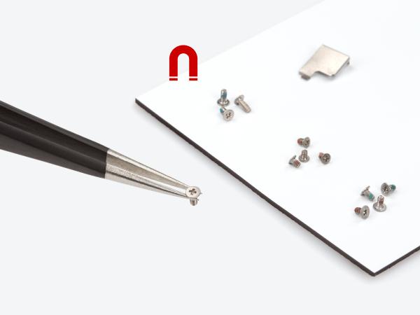 Tekton Tweezers holding a small screw above the white magnetic parts mat.